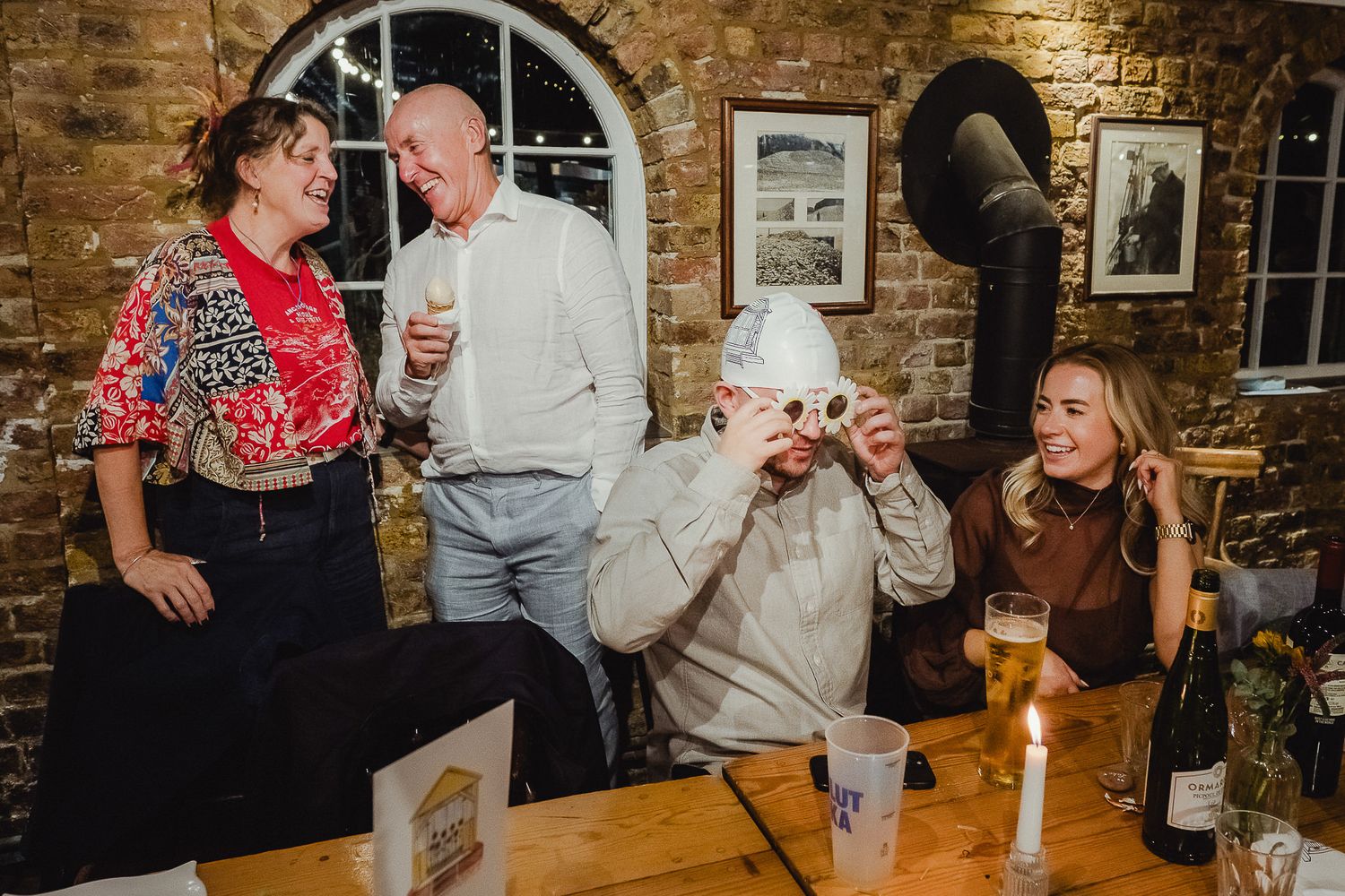 People enjoying drinks and conversation in a cozy brick-walled pub setting.