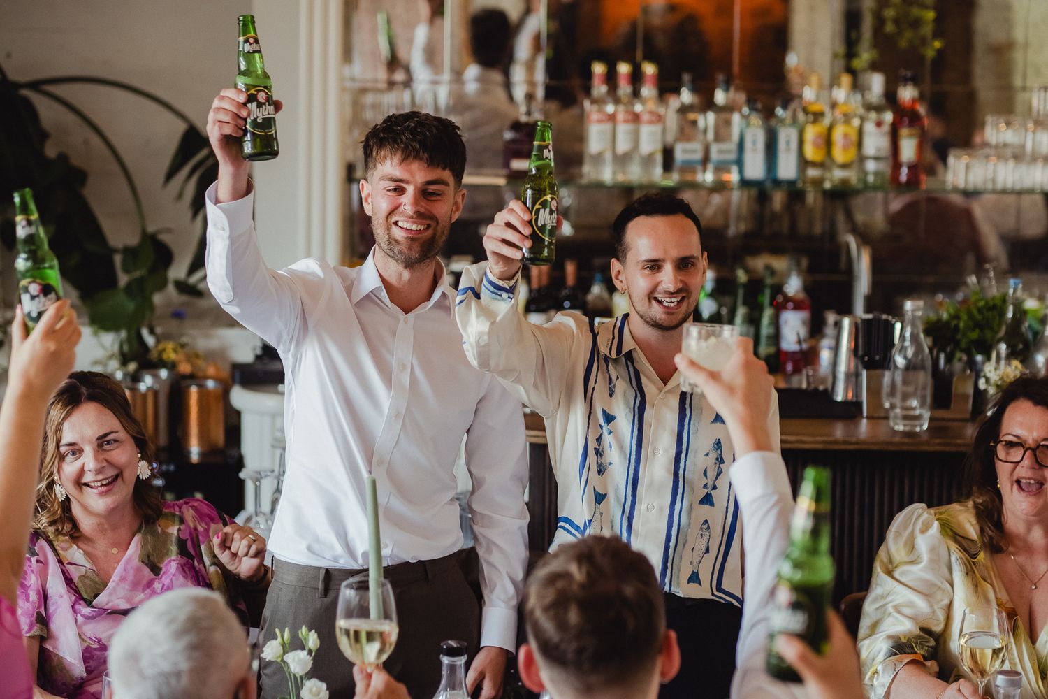People celebrating and toasting with drinks at a lively restaurant gathering.