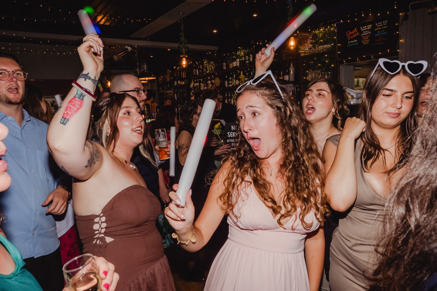 People dancing and celebrating at a lively nightclub party with colorful lights and drinks.