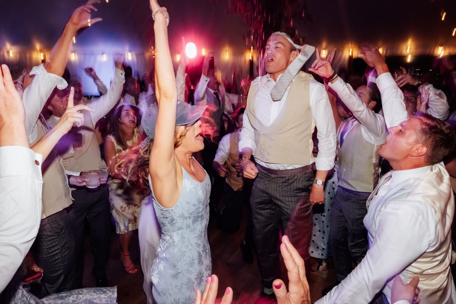 Guests dancing joyfully at a lively wedding reception party with colorful lights.