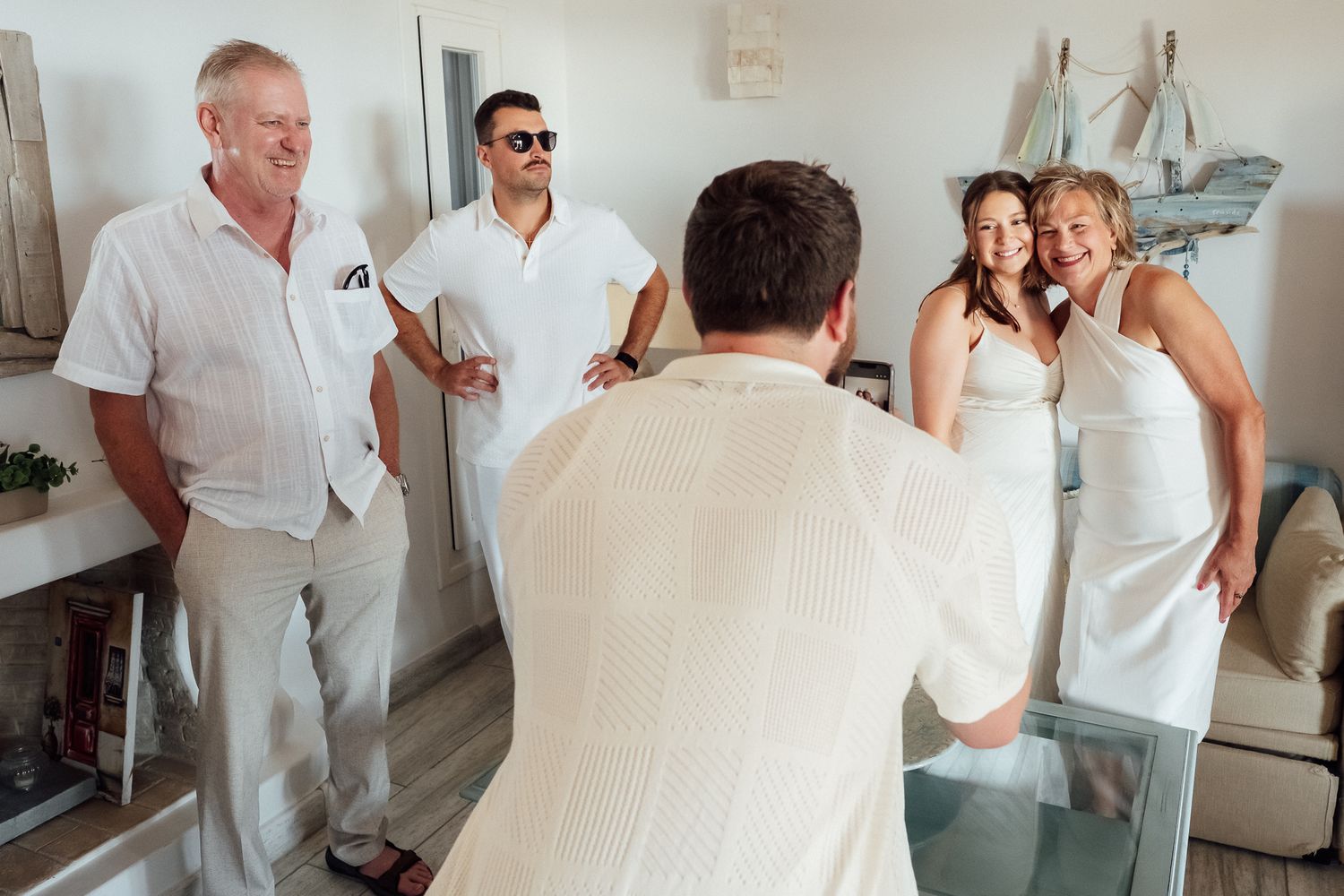 Group of people in white outfits posing for a photo indoors at a bright, casual wedding celebration.