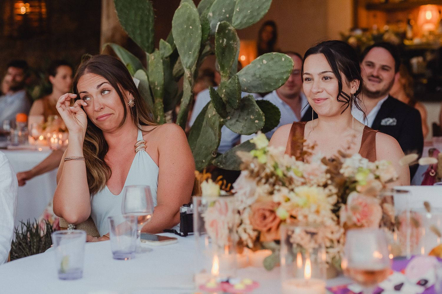Wedding guests seated at elegant reception tables with candlelit centerpieces and floral arrangements.