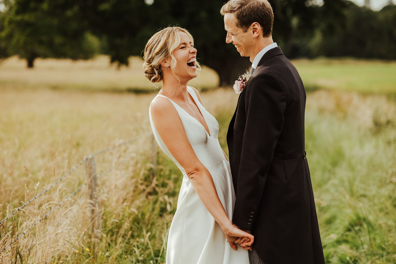 A joyful moment between newlyweds standing in a sun-lit summer field.