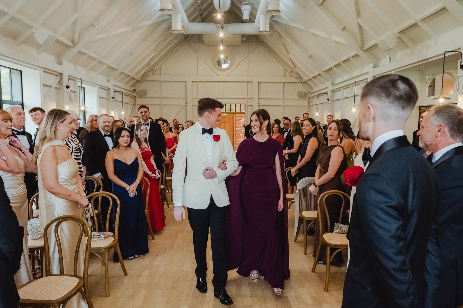 A panoramic view of a wedding reception venue with guests mingling in an elegant white-walled room with vaulted ceilings.