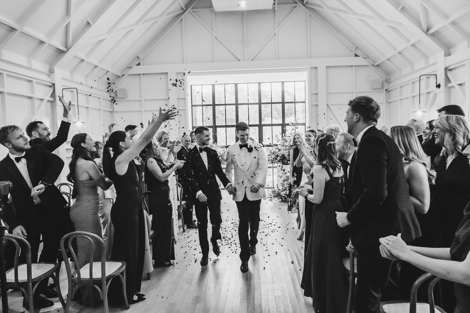 Wedding guests raise their hands in celebration during a joyful reception in a bright, airy venue.