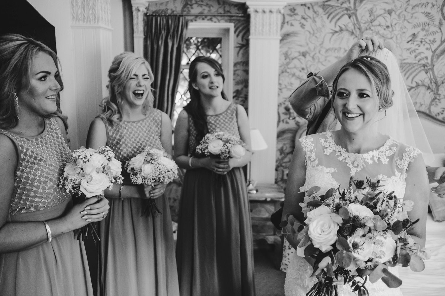 Black and white photo of bridesmaids in matching dresses sharing joyful moments with the bride.