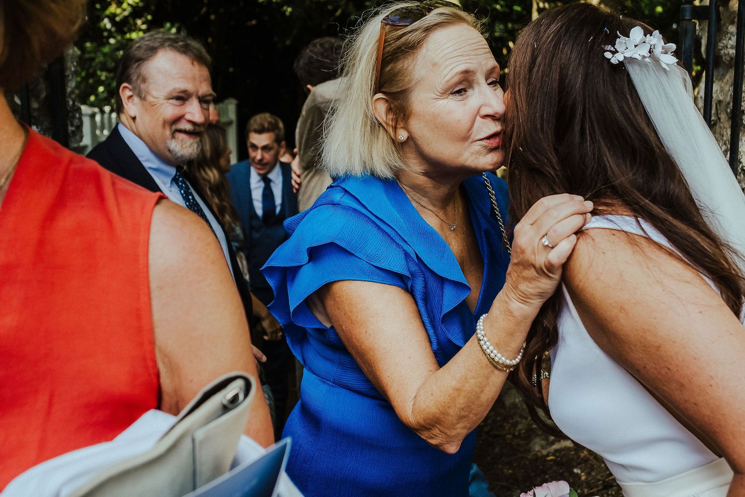 A joyful celebration at an outdoor wedding reception with guests in bright formal attire.