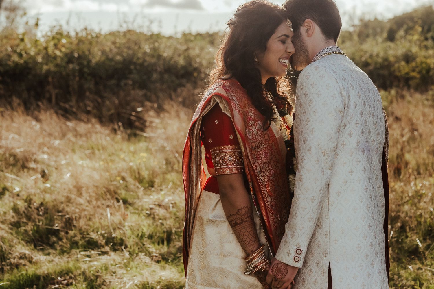 Intimate moment between newlyweds in traditional Indian wedding attire at sunset.