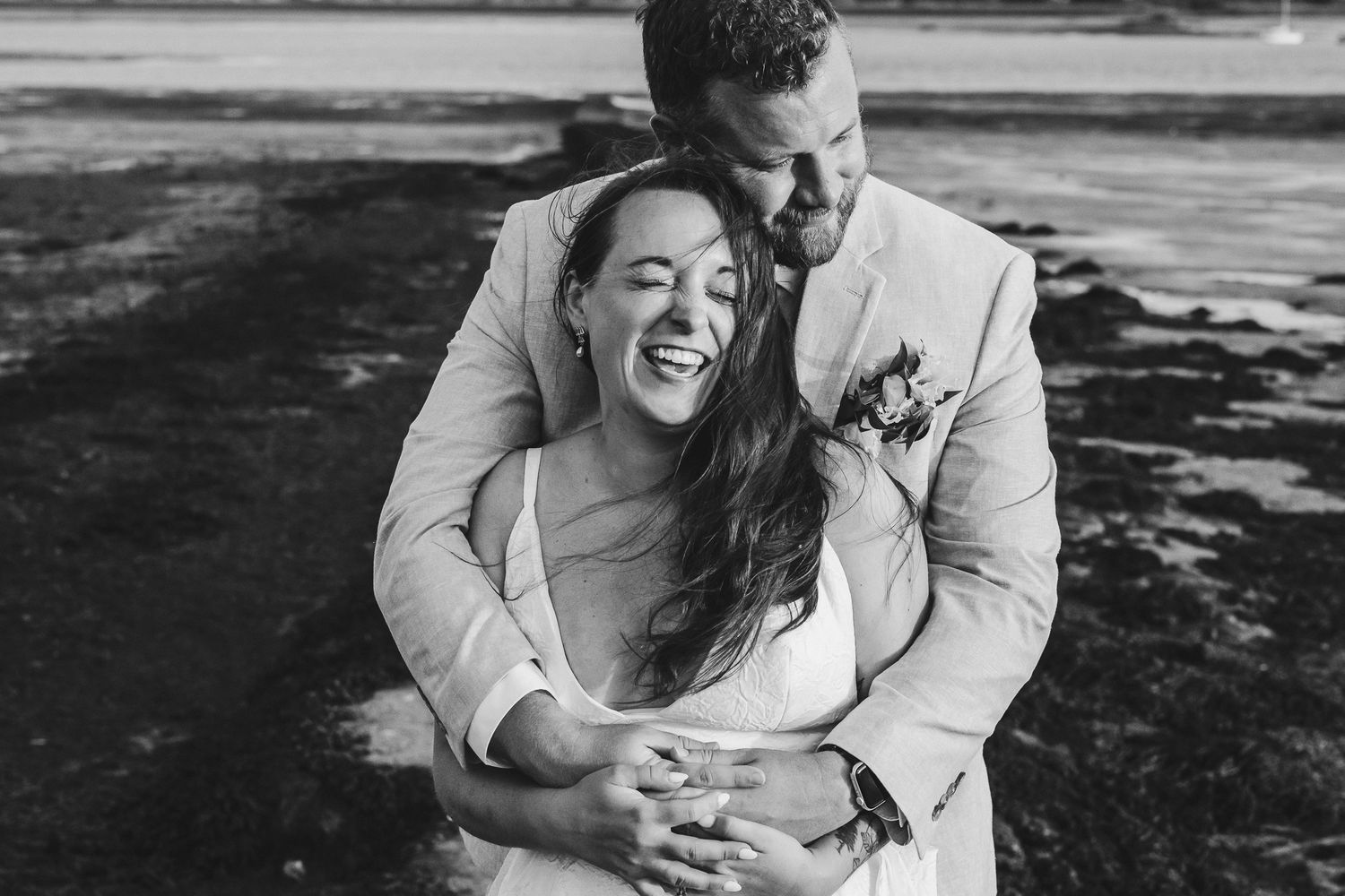 A joyful couple shares a candid embrace during their black and white wedding photoshoot outdoors.