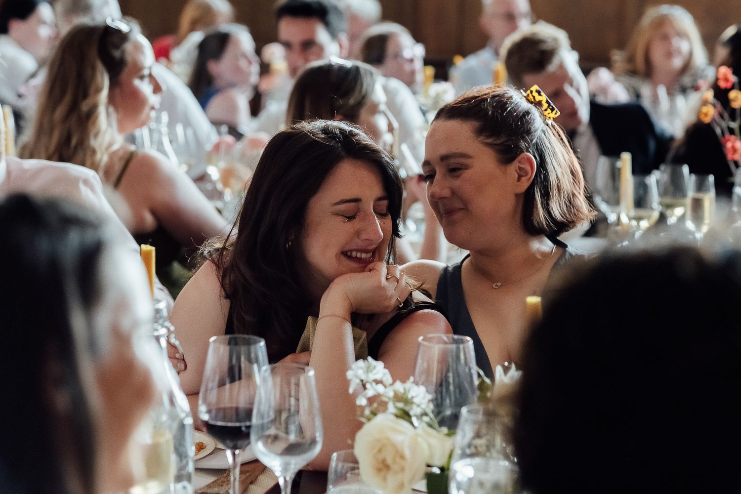 Two women laughing and sharing a joyful moment at an elegant wedding reception dinner.