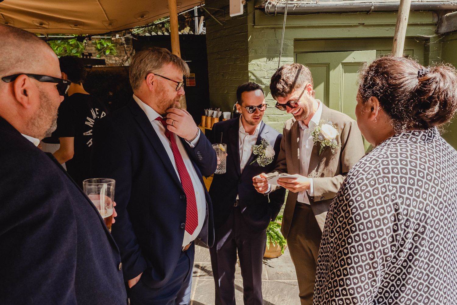 Wedding guests gather at an outdoor reception venue, mingling and socializing under a covered patio area.
