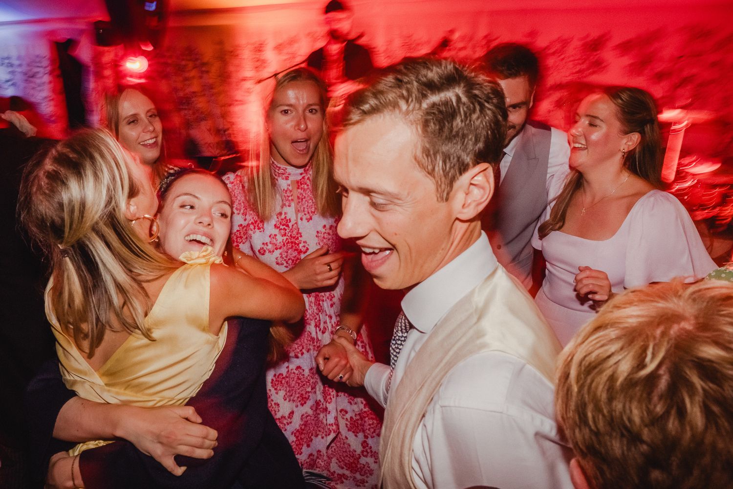 People dancing and celebrating at a party with vibrant red lighting and a festive atmosphere.