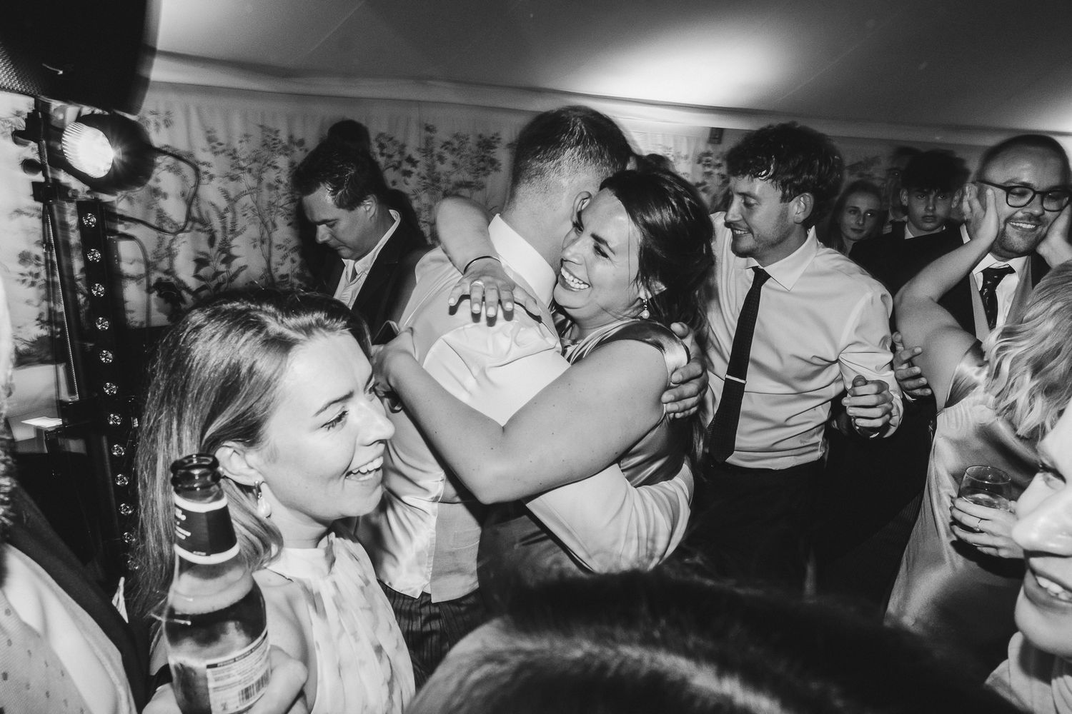 Black and white photo of people dancing and celebrating at a lively party with drinks in hand.
