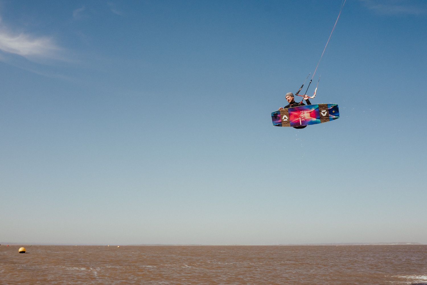 A kitesurfer performs aerial maneuvers over choppy ocean waters against a bright blue sky.