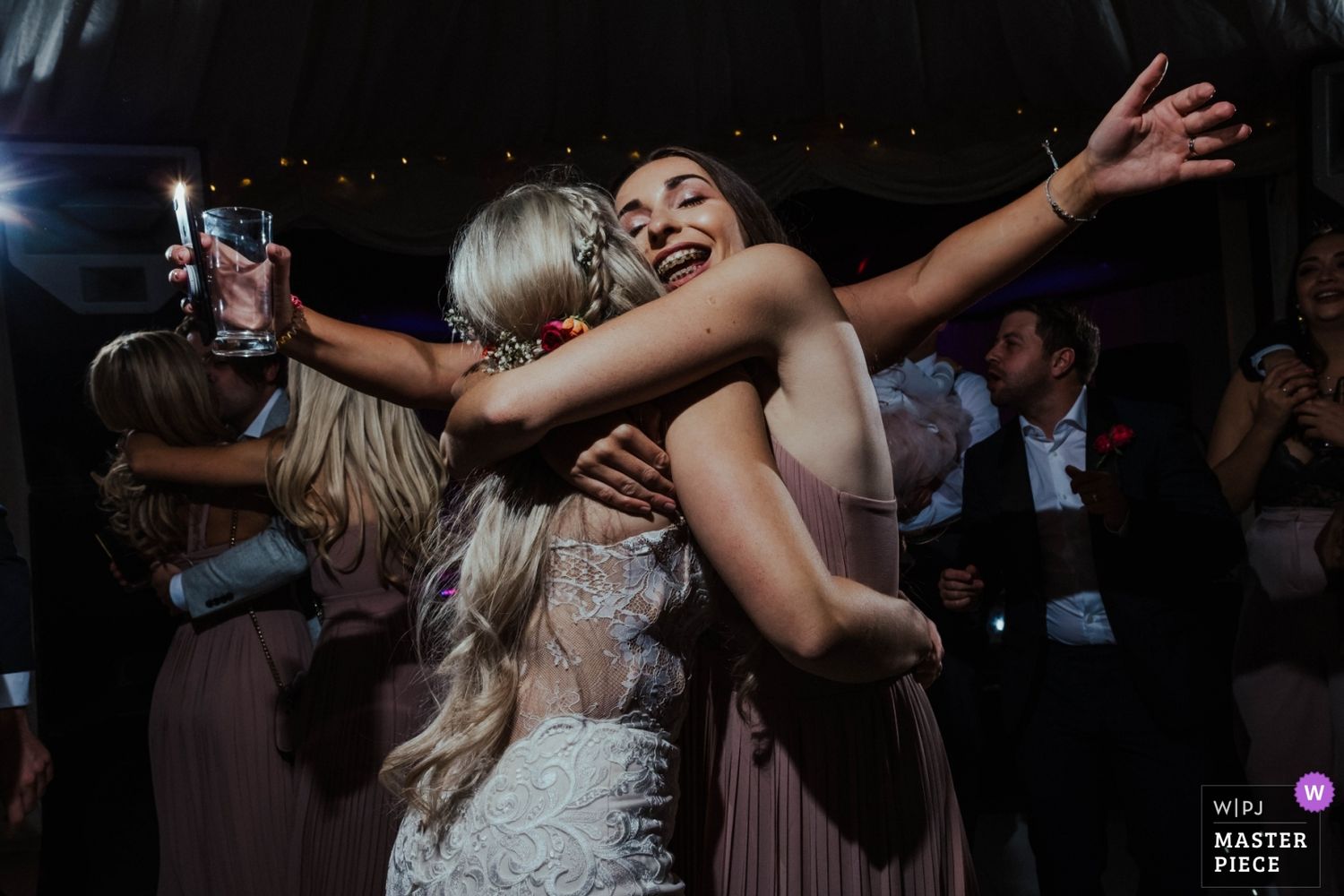 Wedding party dancing and celebrating on a dark dance floor with dramatic lighting.