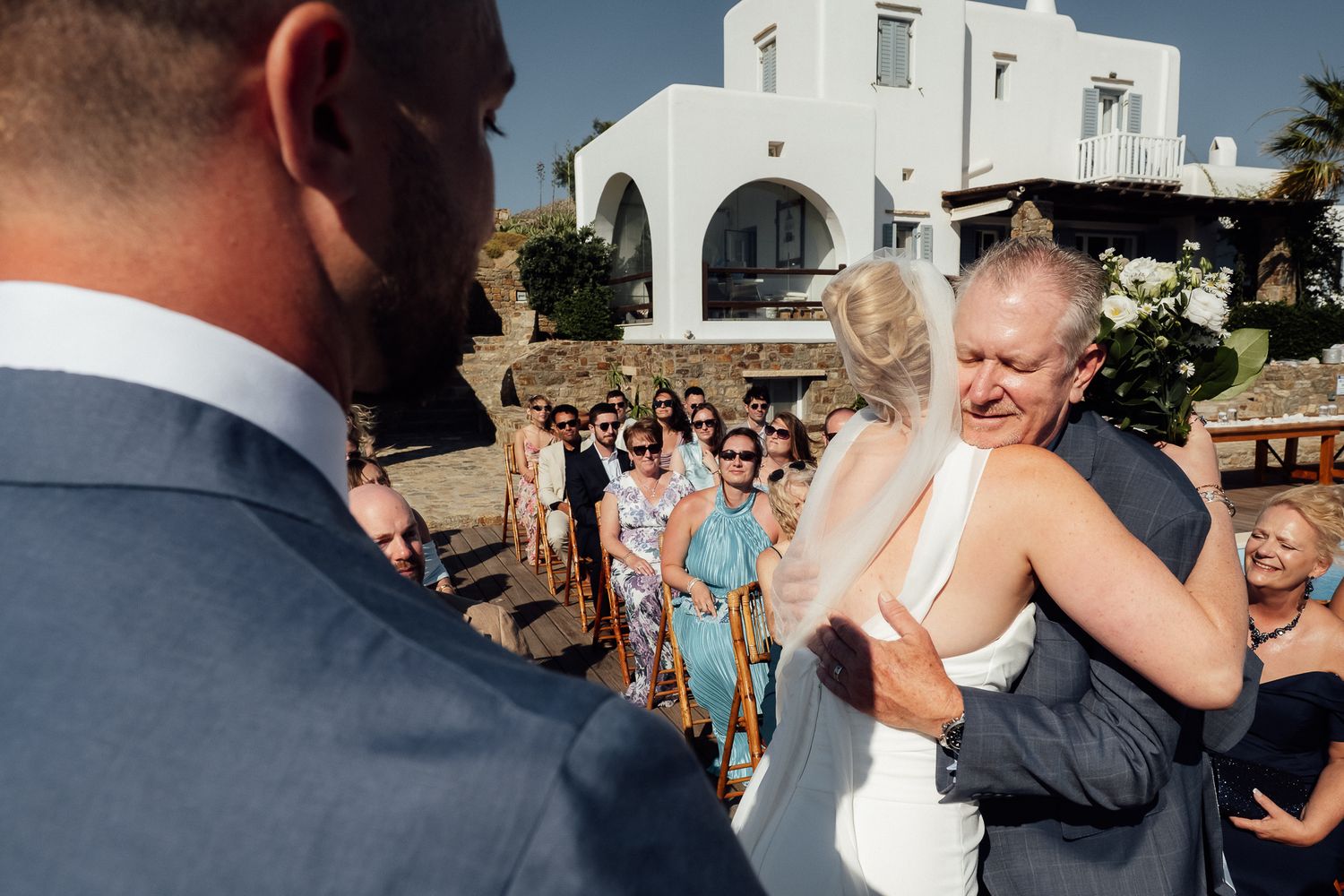 Bride and groom sharing an emotional hug during outdoor wedding ceremony in Santorini Greece with guests watching.