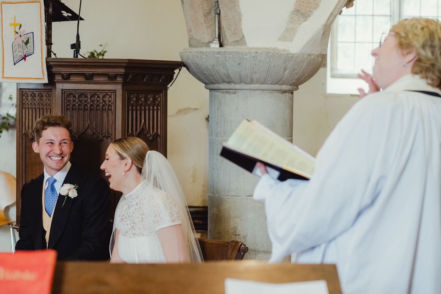 A joyful moment during a wedding ceremony in a church as participants share laughter with the officiant.