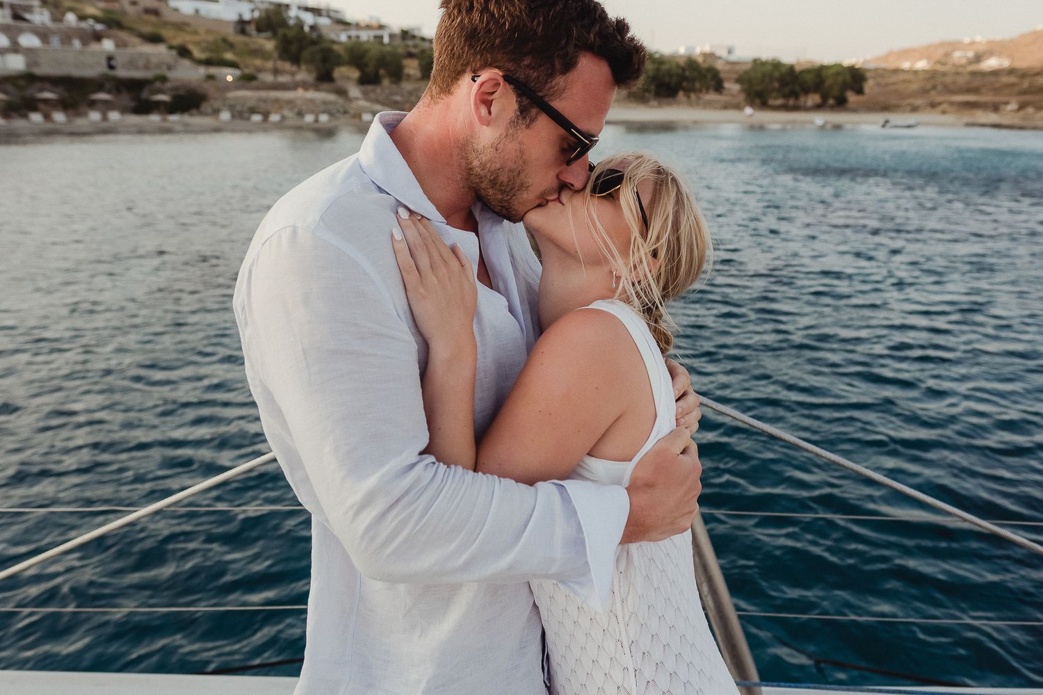 A romantic series of images showing a couple sharing tender moments and kisses on a boat at sea during sunset.