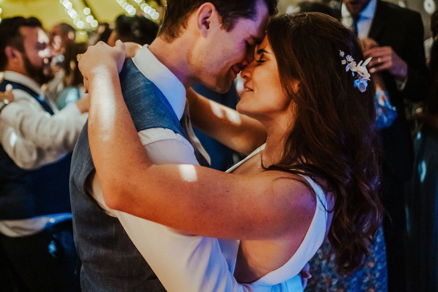 A couple shares an intimate dance at their wedding reception with guests in the background.