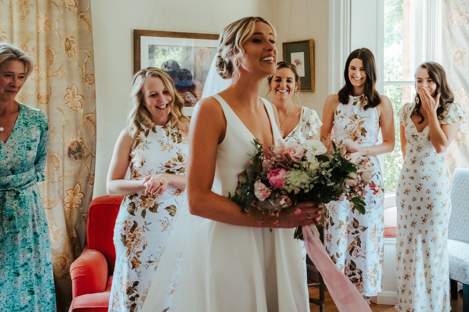 A joyful bride holding a bouquet surrounded by bridesmaids in floral print dresses.