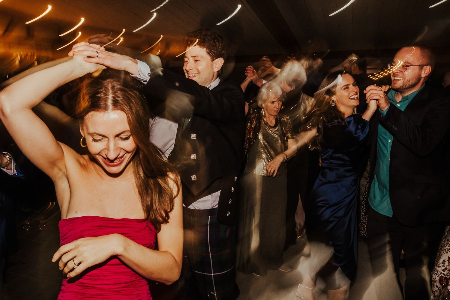 People dancing enthusiastically under dim lighting at a wedding reception party.