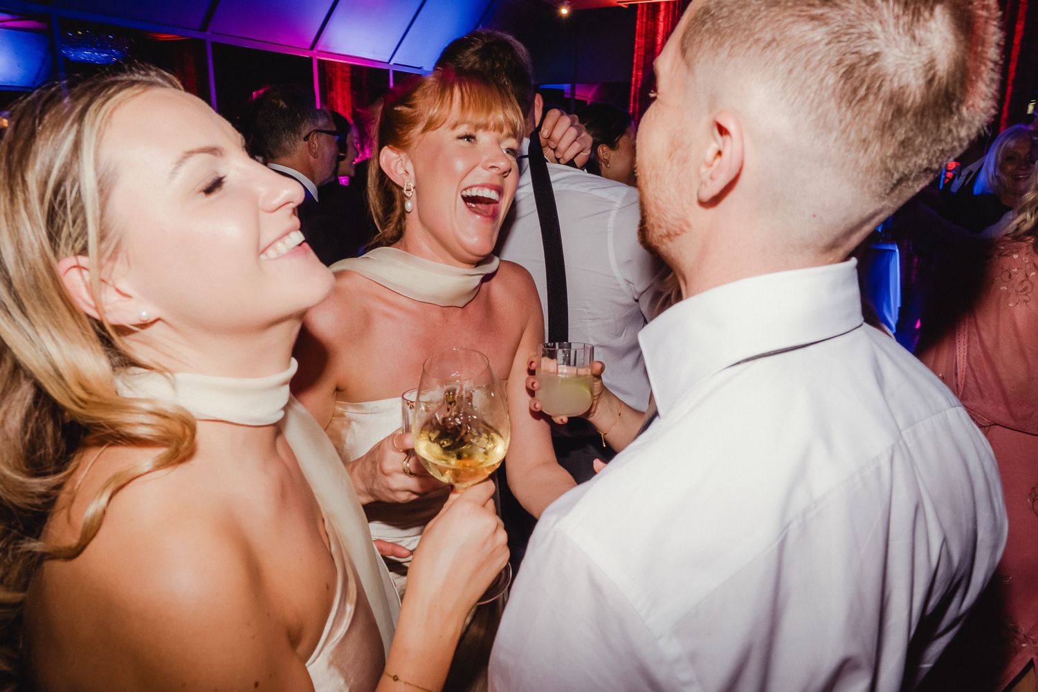 People dancing and celebrating at a lively wedding reception with colorful purple lighting and a festive atmosphere.