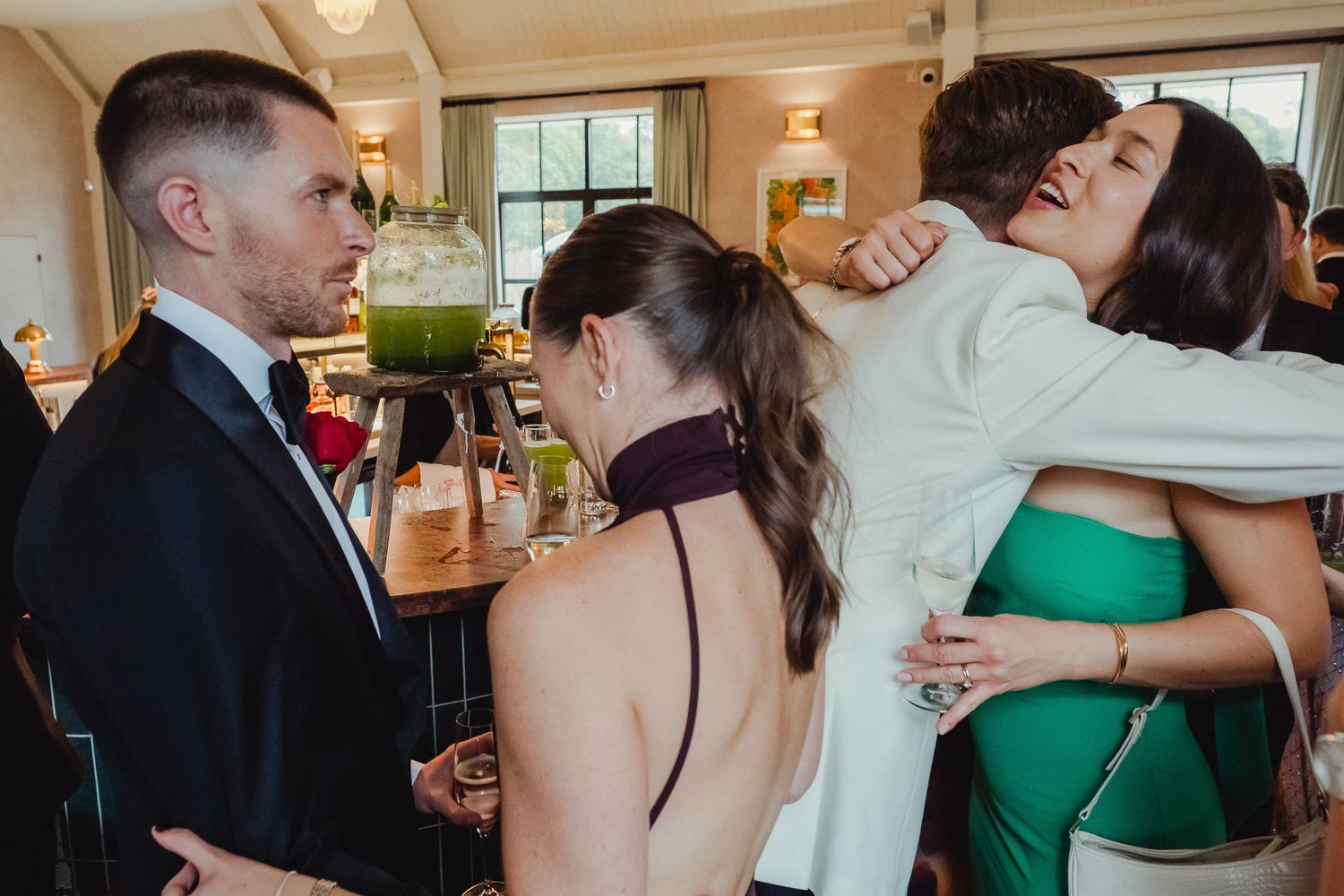 Wedding guests share warm embraces and conversations during a reception in an elegant indoor venue.