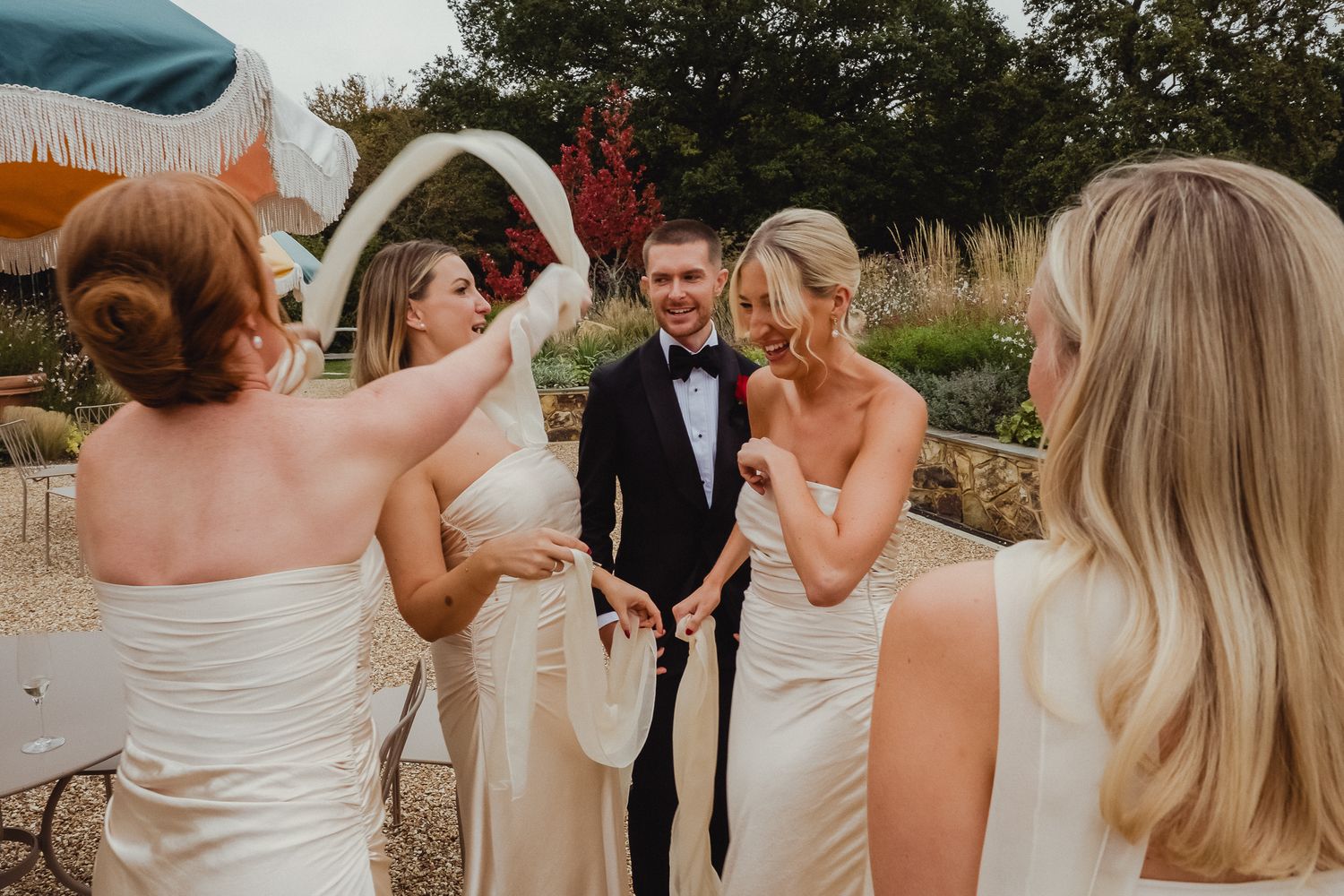 A wedding party laughs together during a candid moment in an outdoor garden setting.