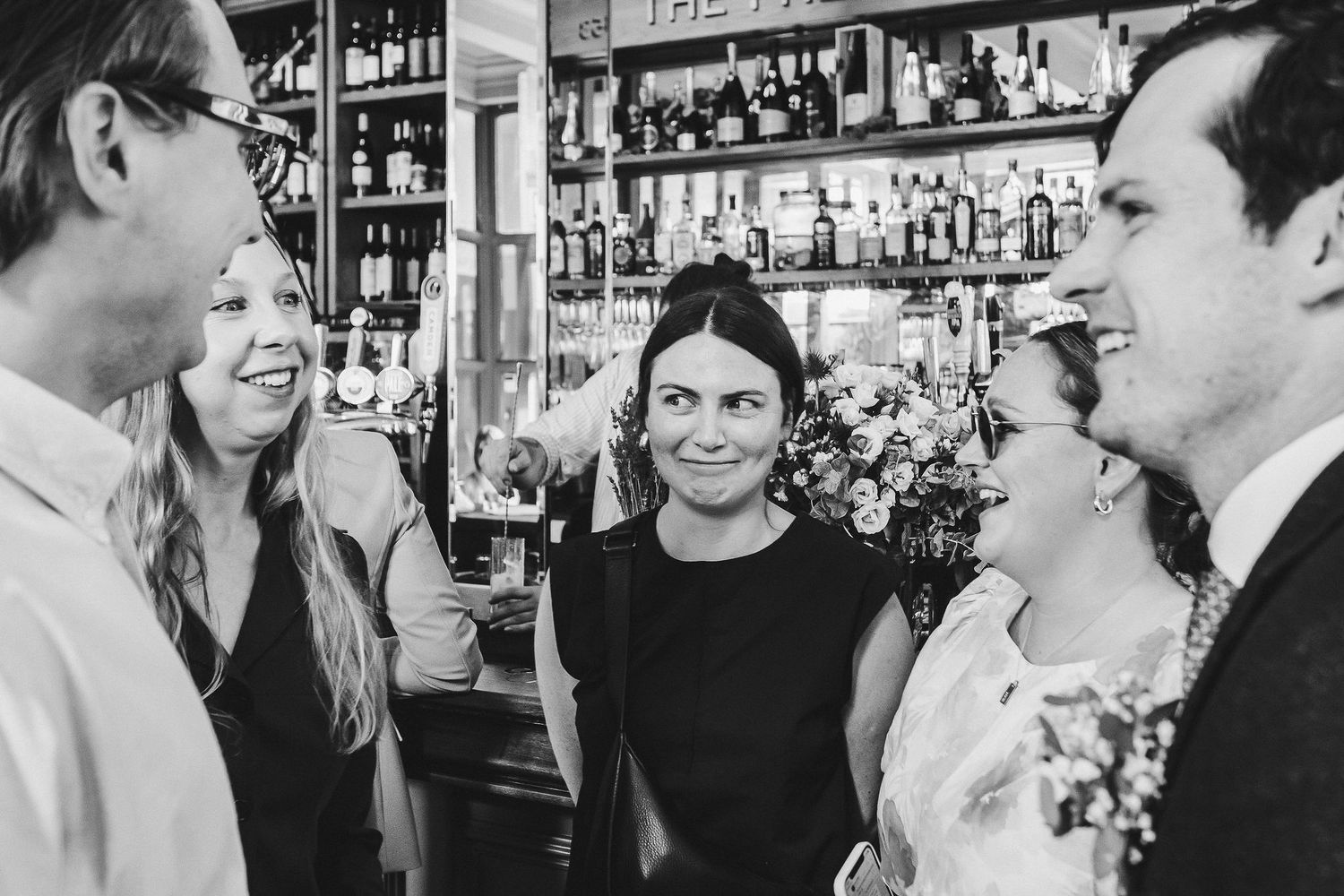 Black and white wedding photos show intimate moments between couples at a bar with bottles and glassware in background.