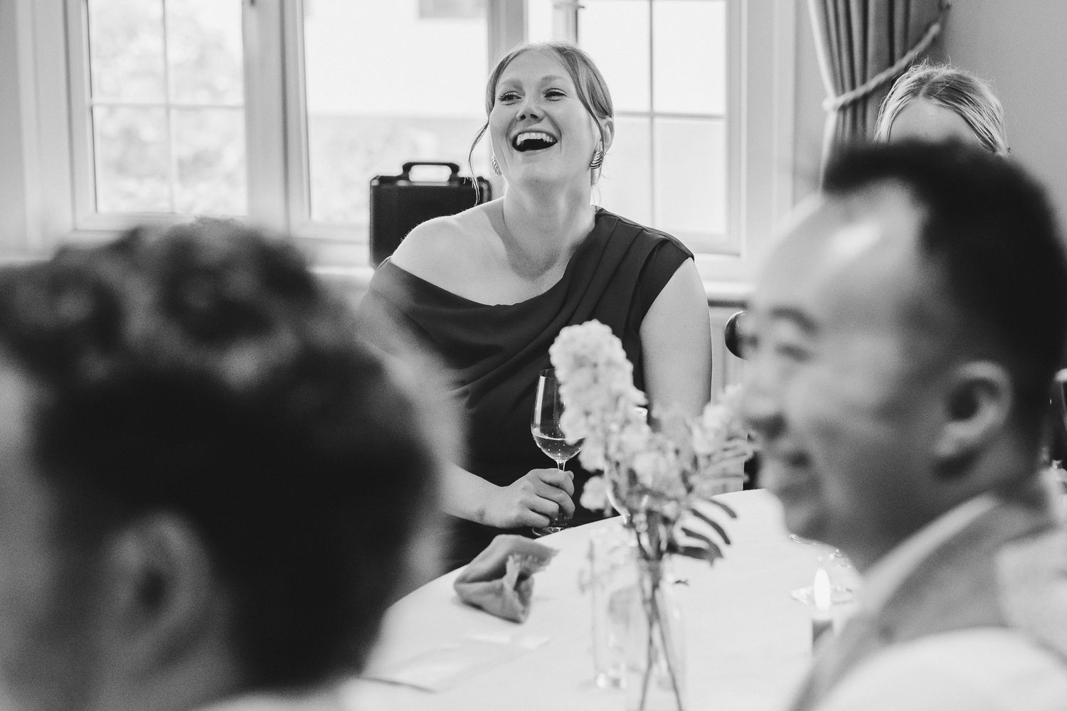 A group of wedding guests share a joyful moment of laughter during a reception celebration.