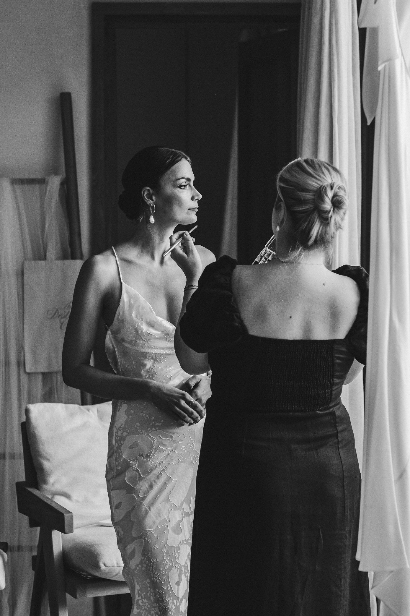 Black and white photo series showing bride and bridesmaid getting ready in formal dresses before wedding ceremony.