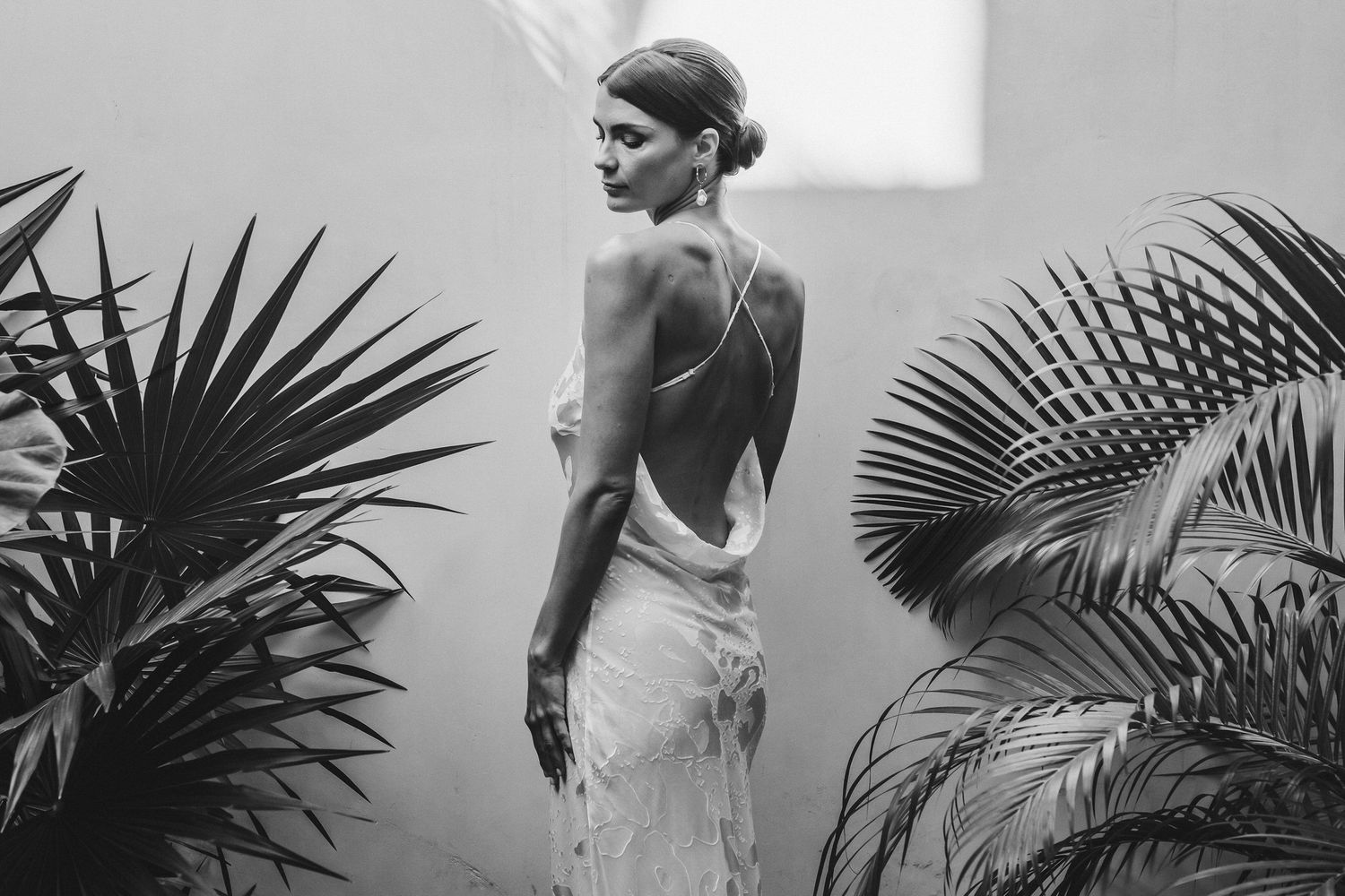 Black and white fashion photograph with elegant poses against a backdrop of tropical palm leaves and shadows.