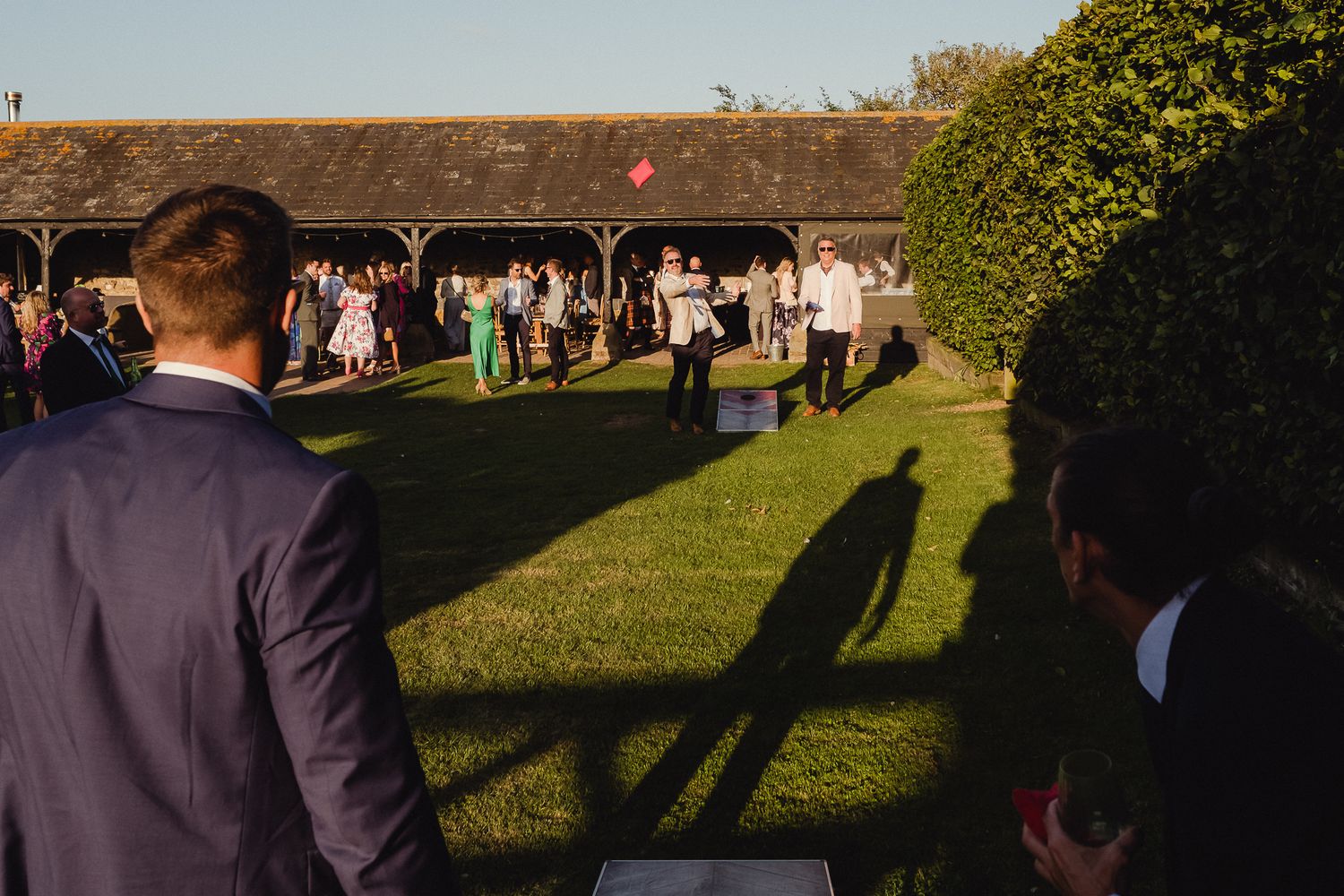 Wedding guests gather on a sunny lawn during an outdoor reception celebration.