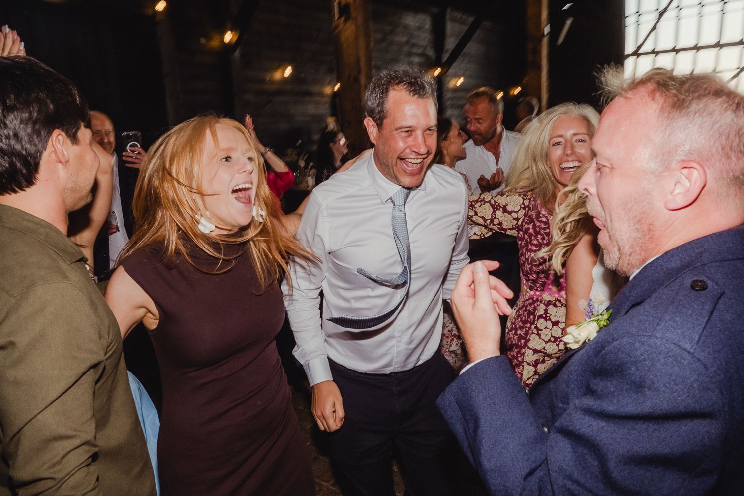 People dancing and laughing together at a lively party celebration with warm lighting in the background.