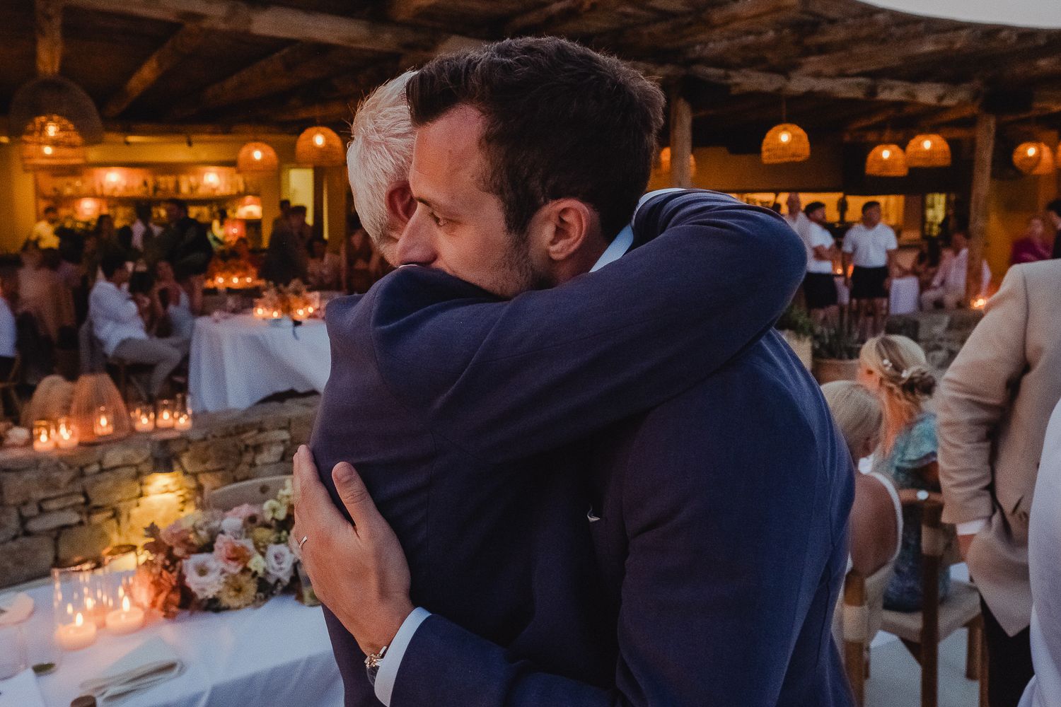 Wedding guests dancing together at an evening reception with warm lighting and candle centerpiece decorations.