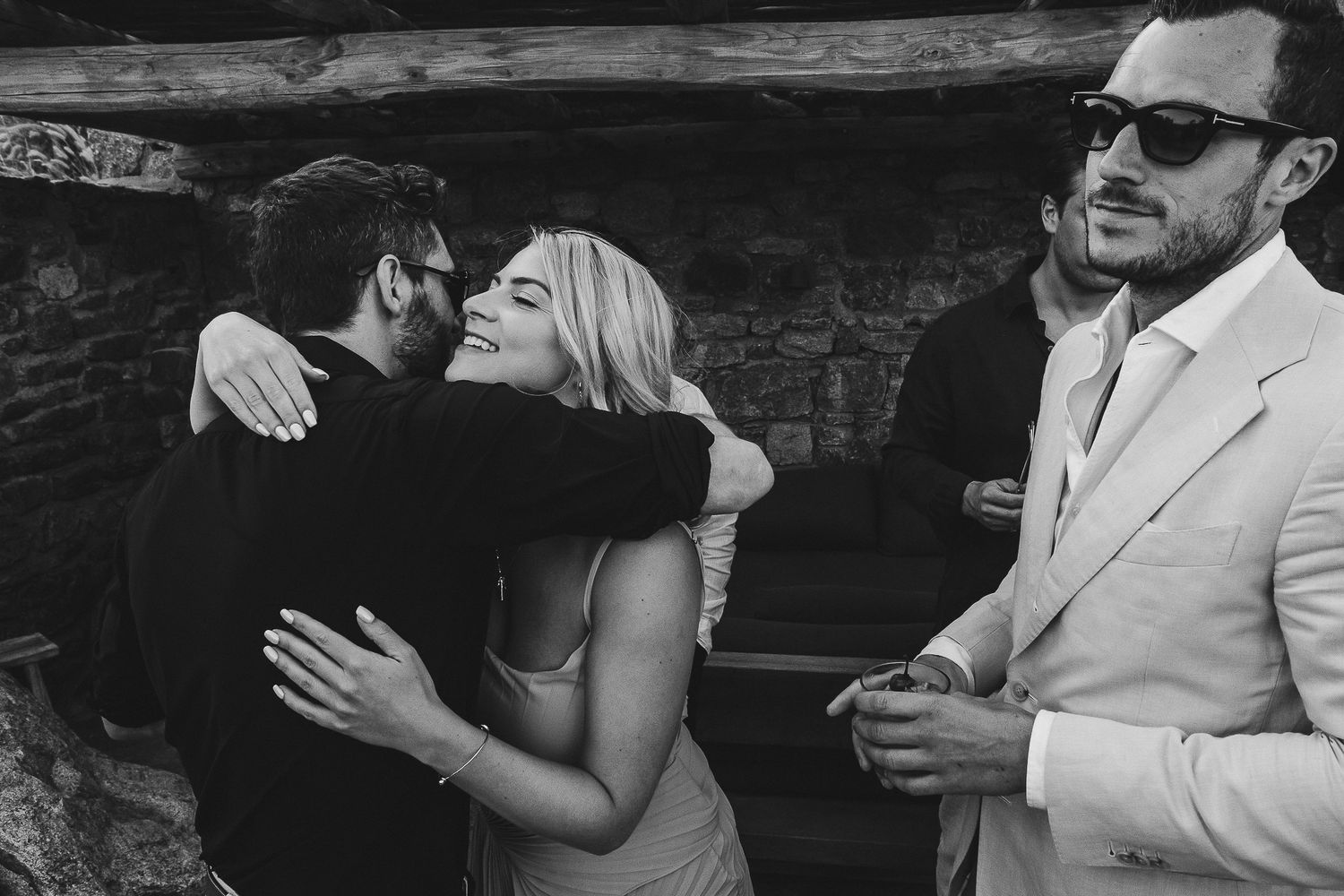 A series of hugs and embraces between party guests celebrating at a dimly lit gathering.