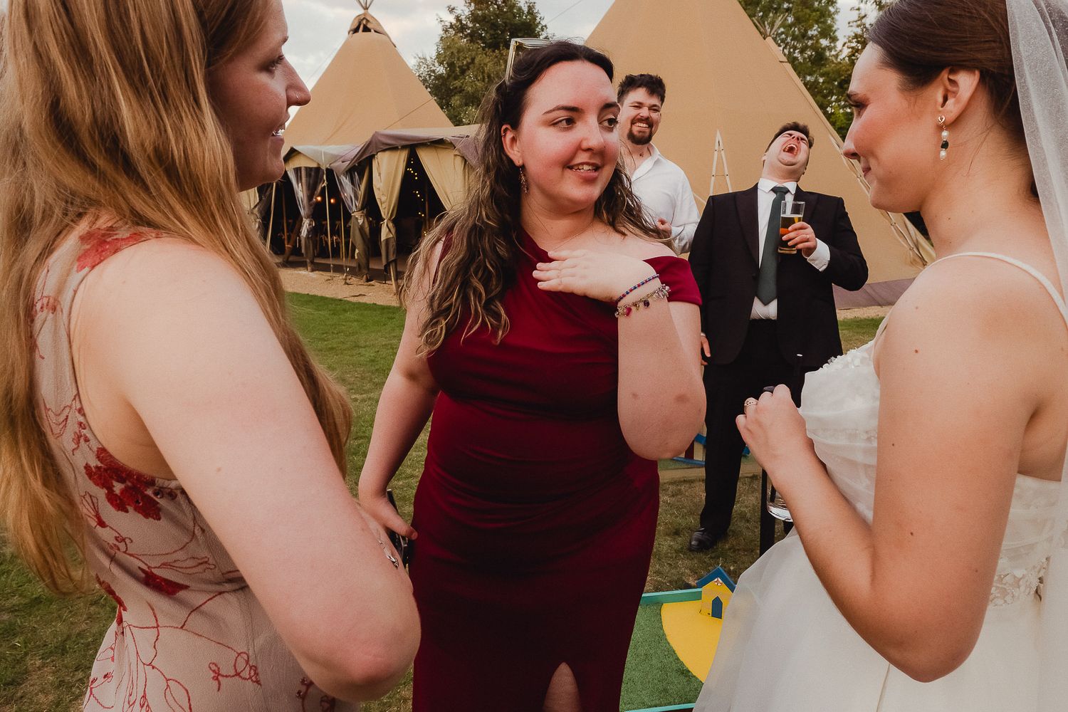 Wedding guests chatting and socializing outdoors with teepee tents visible in the background.