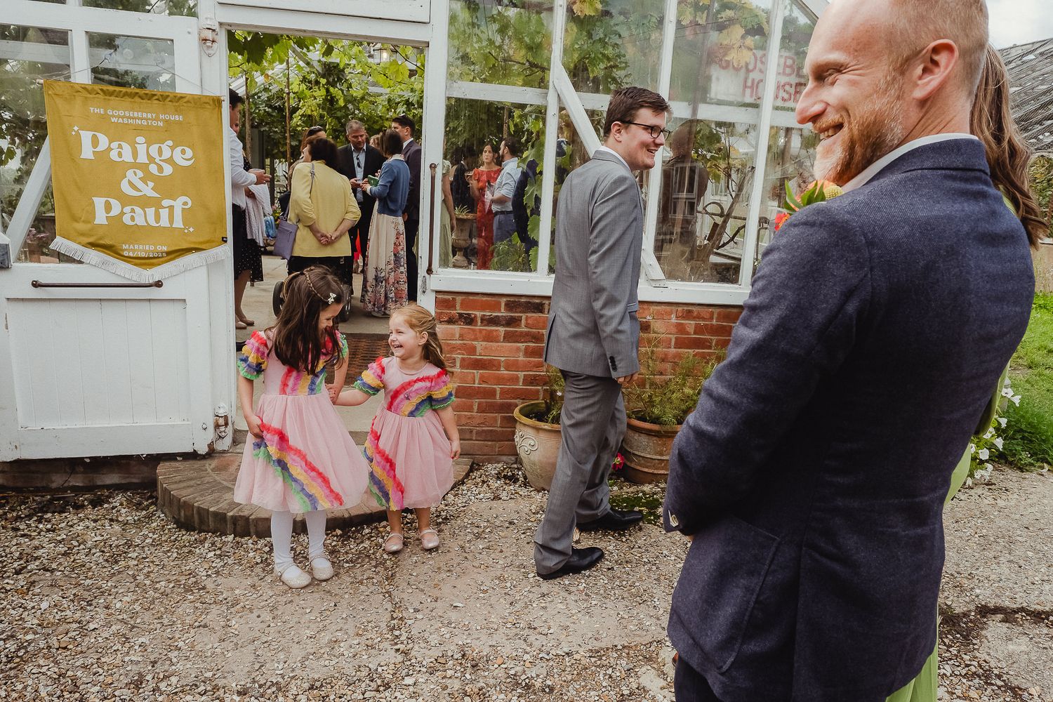 A group of people gather at an outdoor party venue with white decorative elements and string lights.