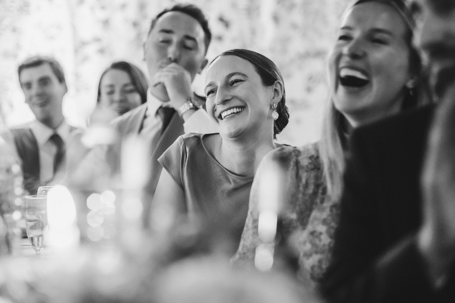 Black and white candid photo of wedding guests laughing and enjoying themselves during a reception.