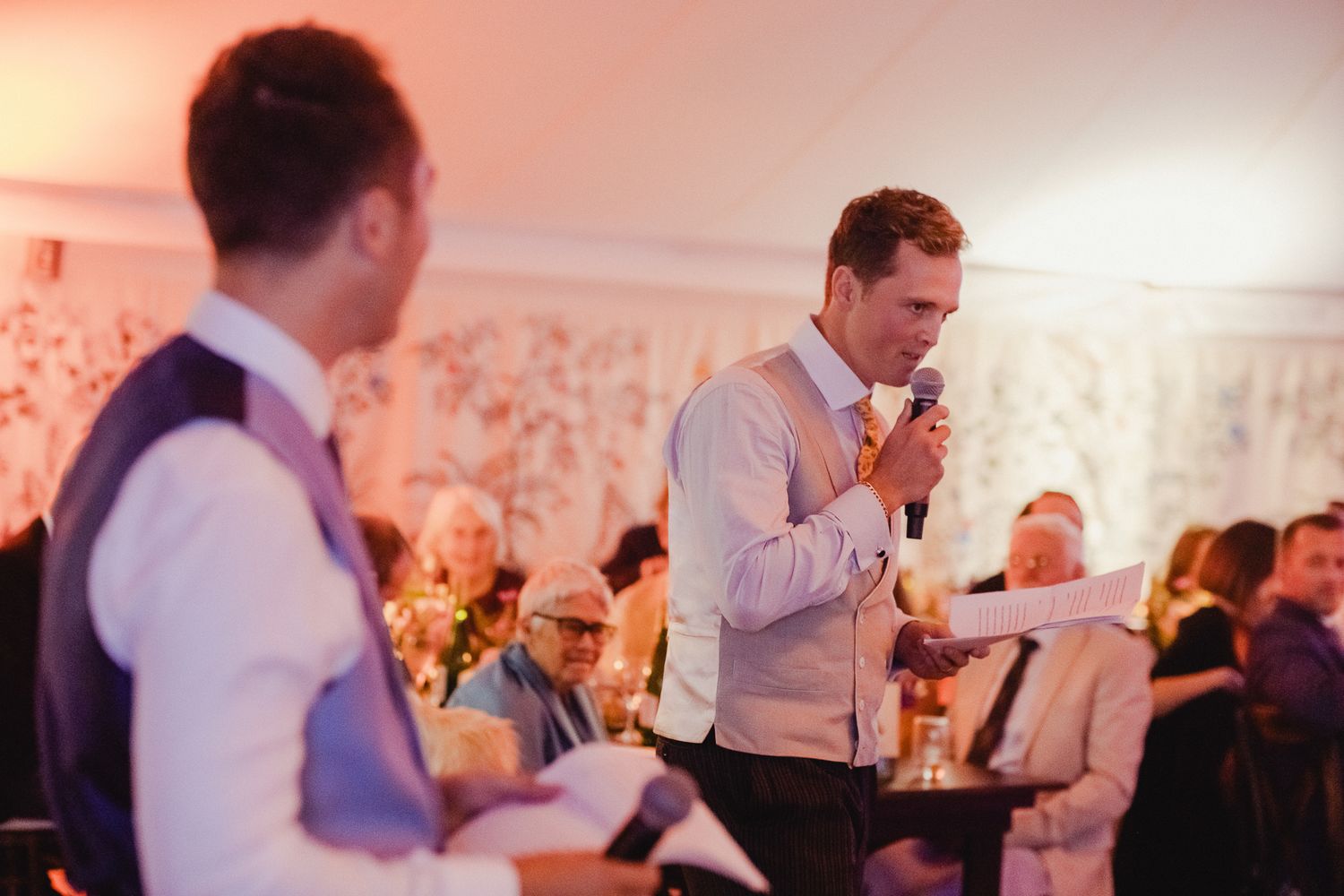 Musicians perform at an indoor wedding reception with warm lighting and floral wallpaper in the background.