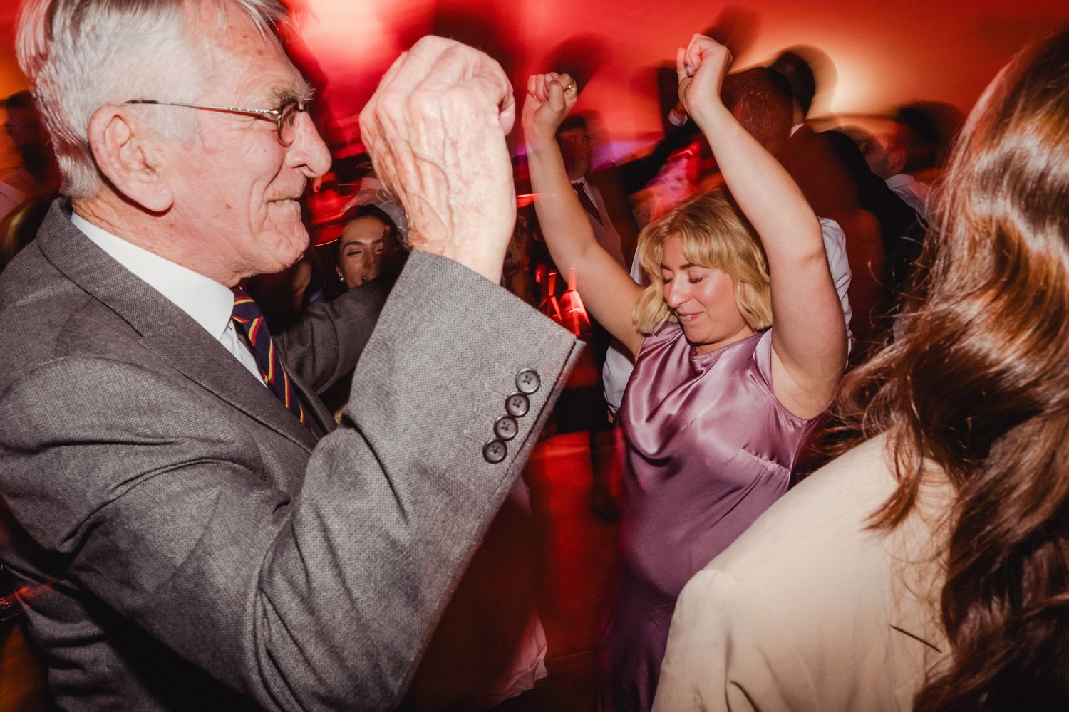 People dancing together at a lively party with red lighting and a festive atmosphere.