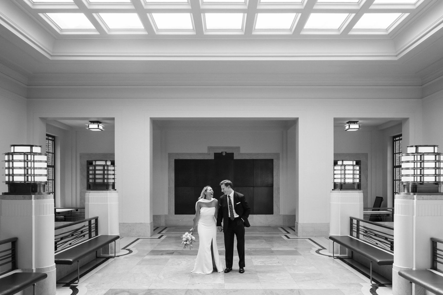 Bride and groom standing together in an elegant wedding venue hall, black and white photo.