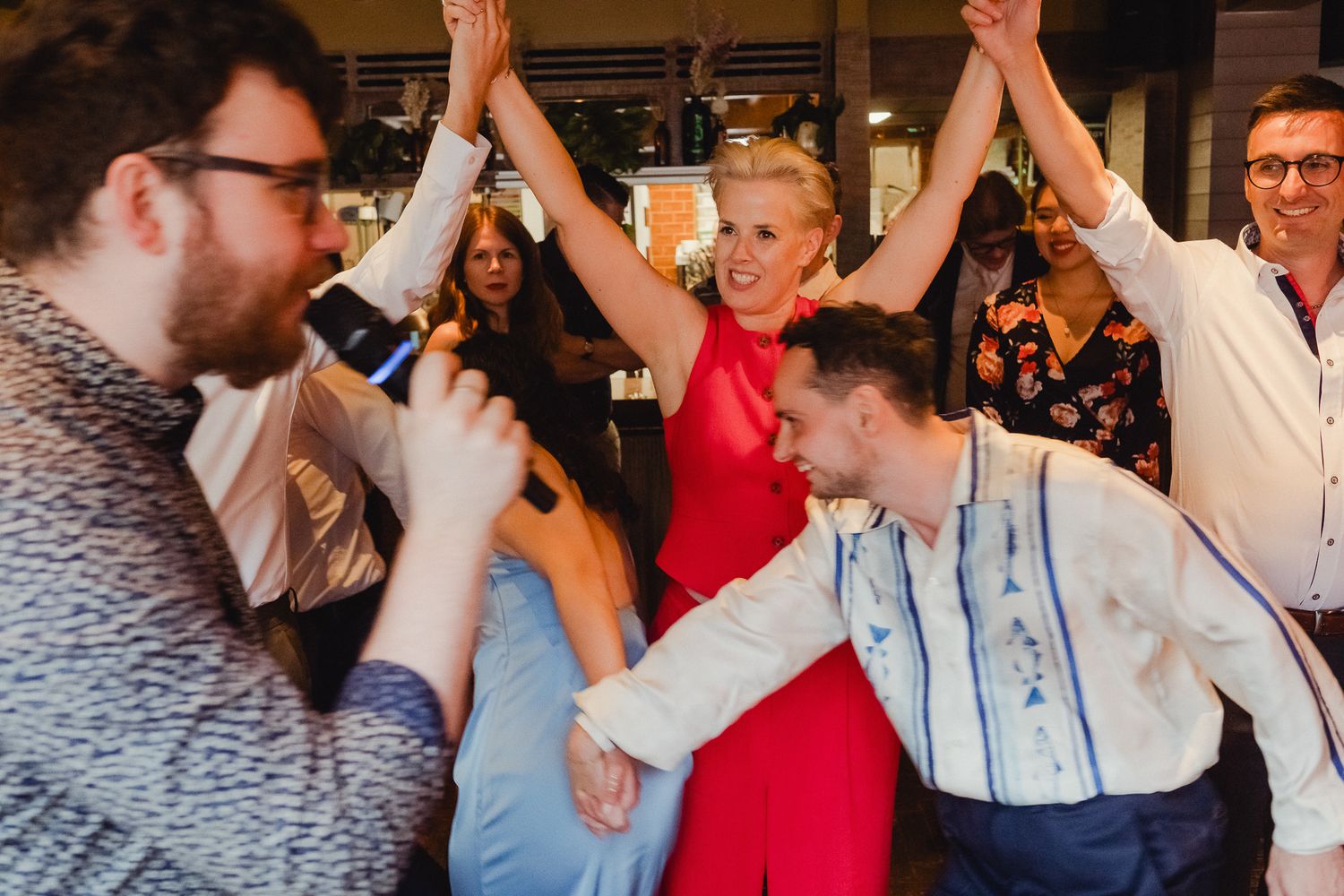 A group of people raise their hands together in celebration at an indoor event.