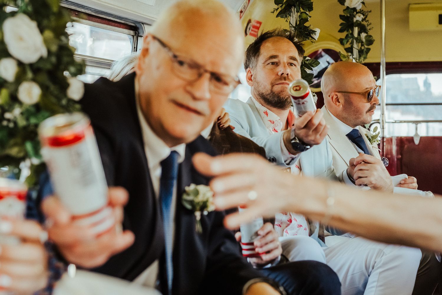 A group holding canned beverages toasts together in celebration at a festive indoor gathering.