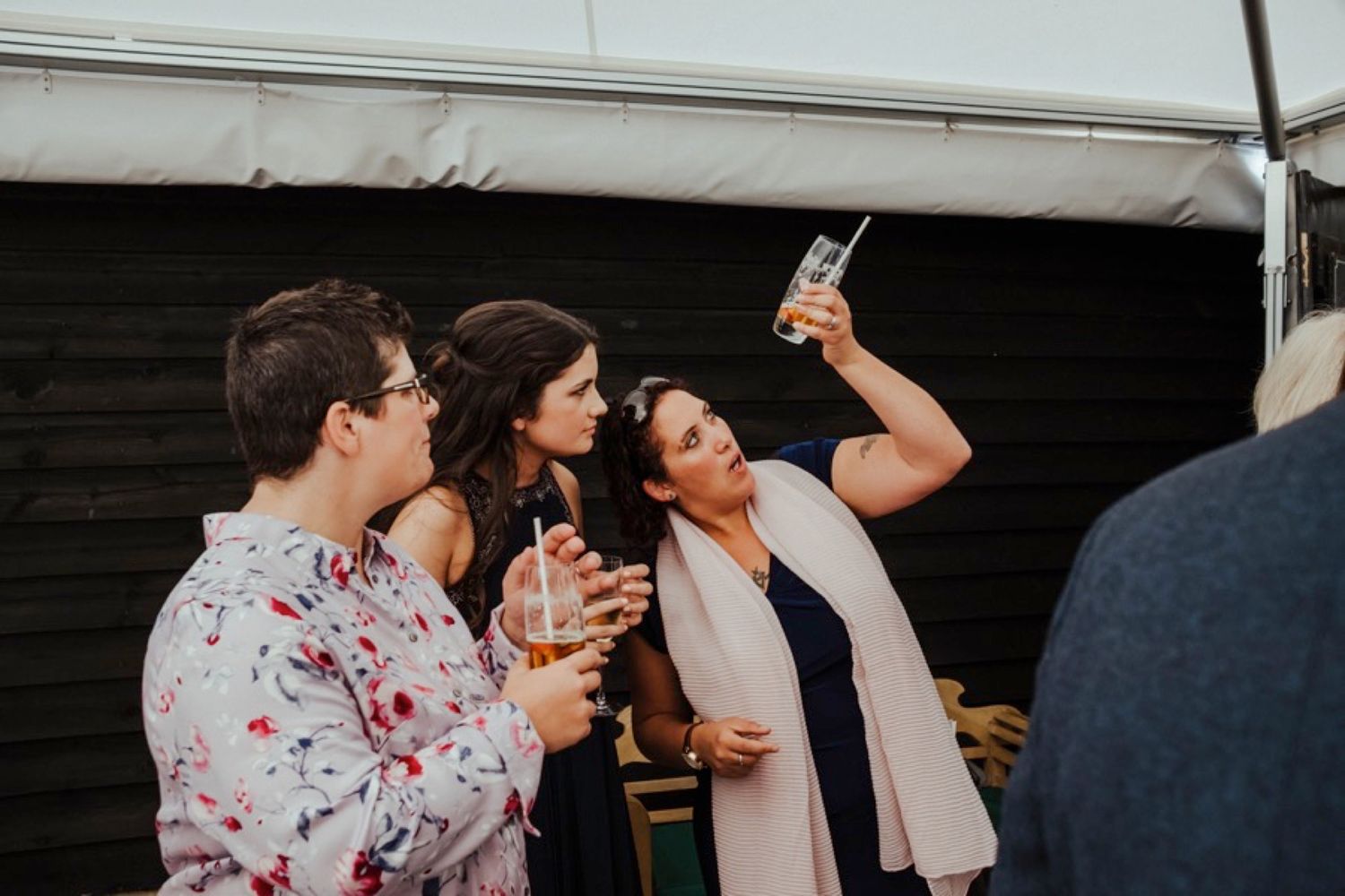 Wedding guests enjoying drinks and laughter at an outdoor reception party.