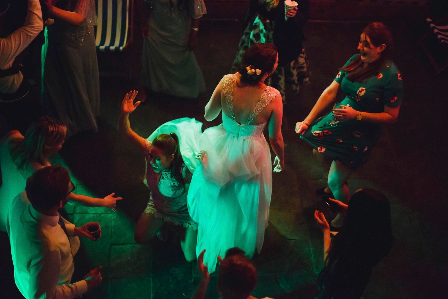 A bride in a white dress dances under green lighting at the wedding reception.