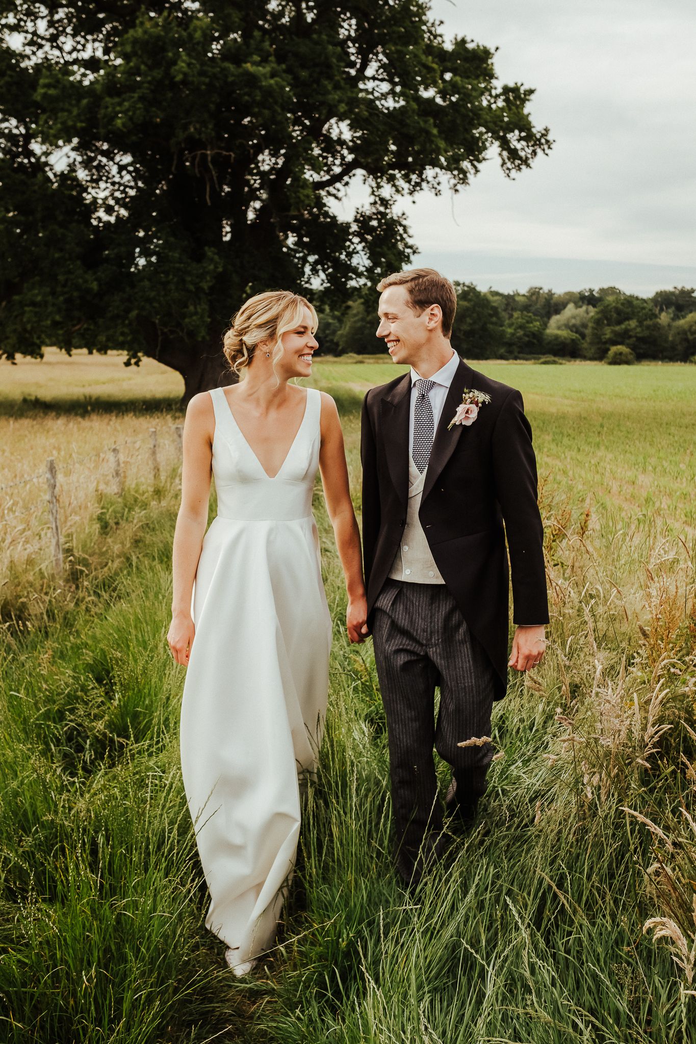A couple walks hand in hand through tall grass in a scenic meadow.