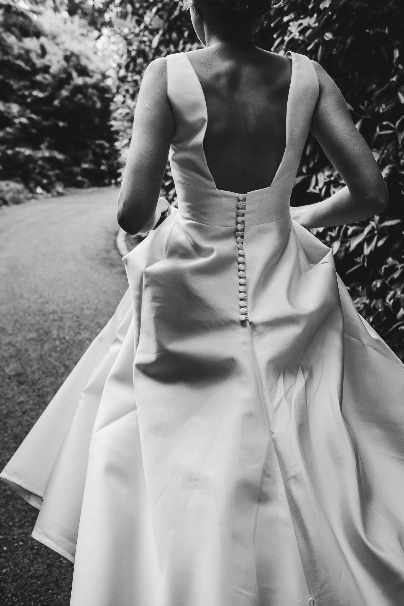 Back view of an elegant white wedding dress with button details on a garden path.