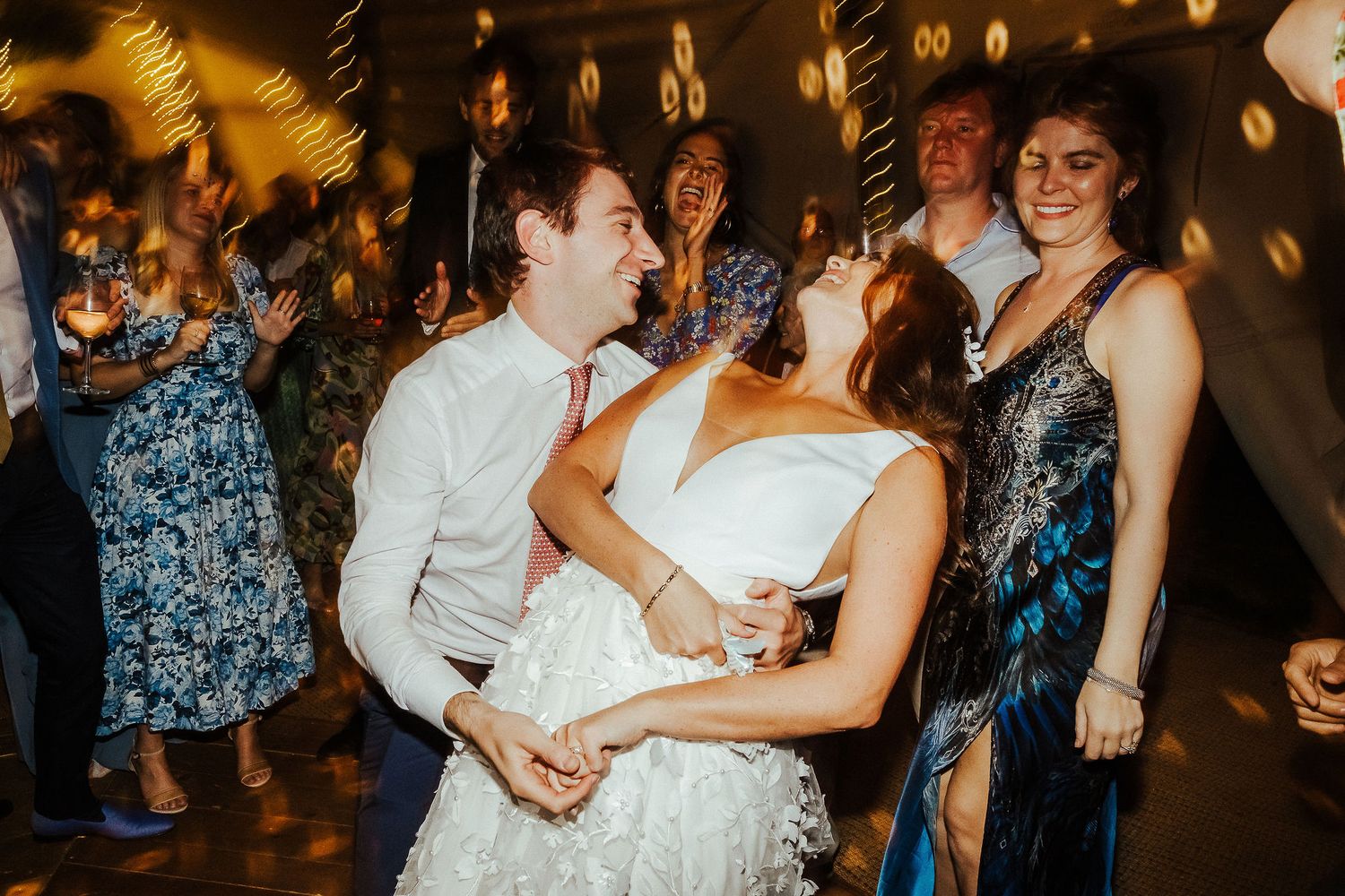 Wedding guests dancing and celebrating on a dimly lit dance floor with festive lighting.