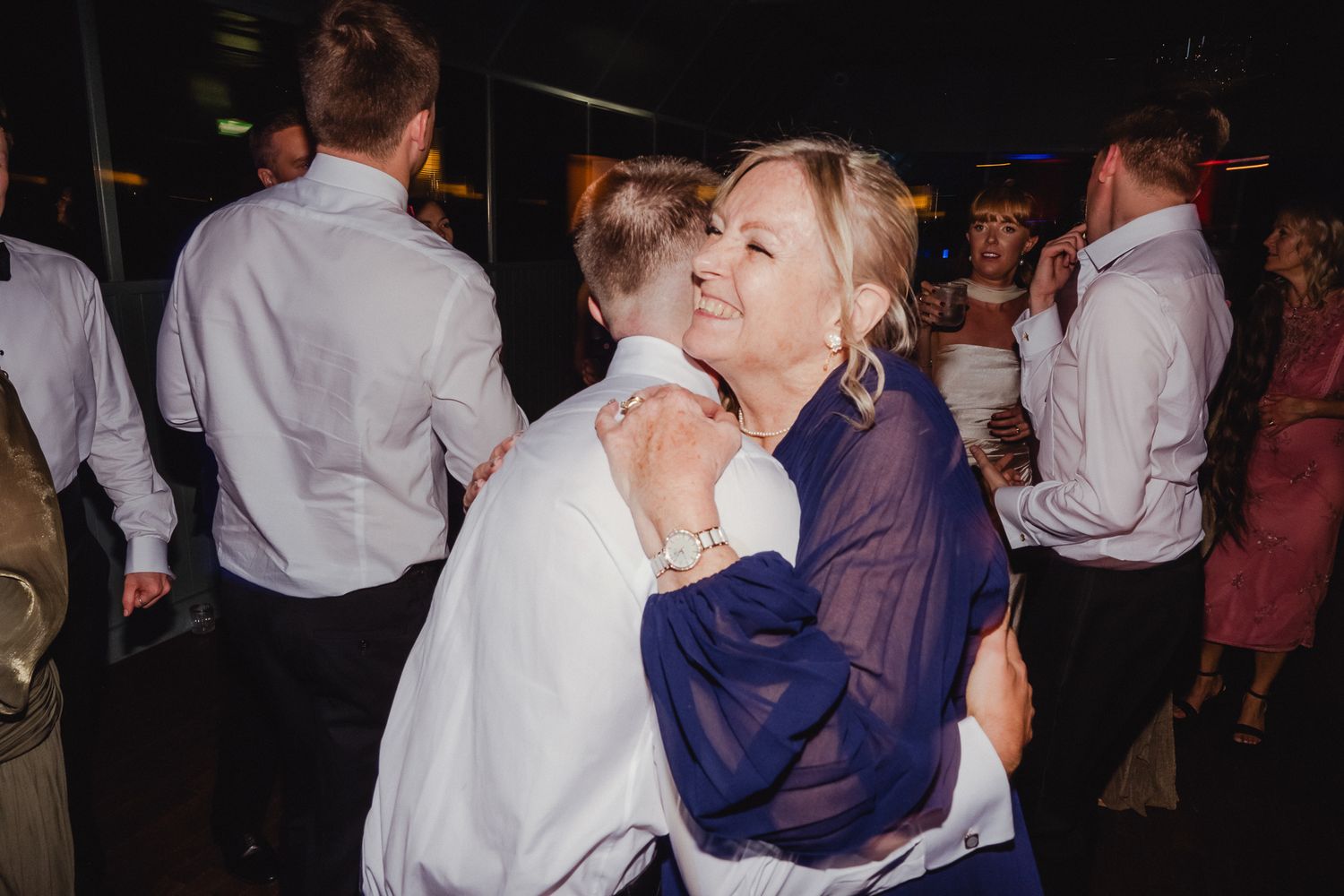 Couples dance together at a dimly lit wedding reception or party venue.